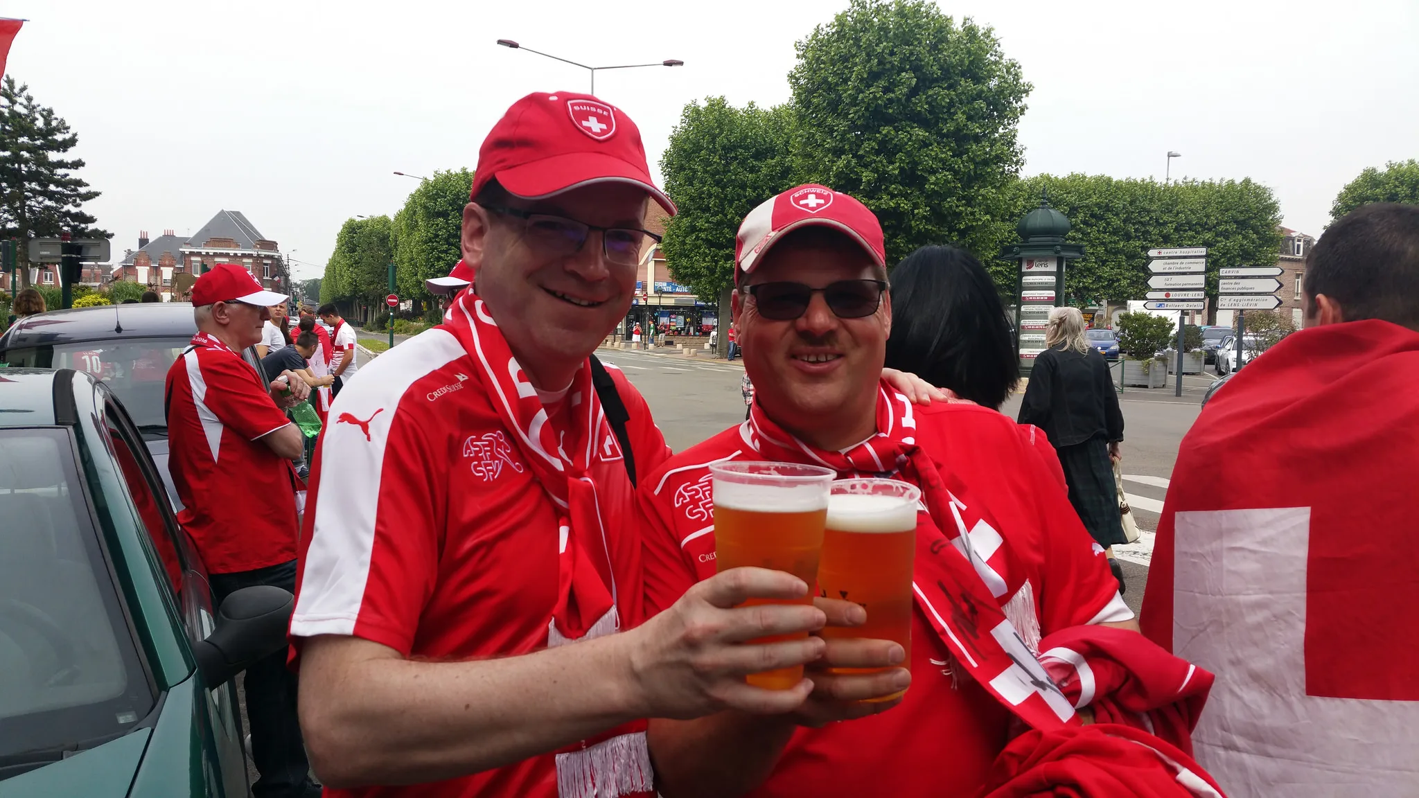 Zwei Fans in Schweizer Trikots und Kappen stossen auf der Strasse mit Bier an