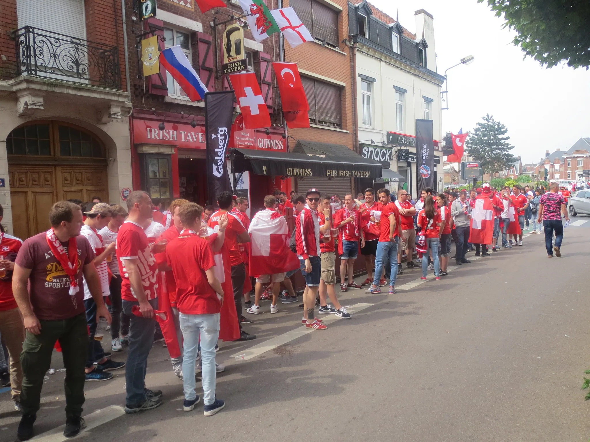 Fans in roten Trikots vor einem Pub in Lens an der EM 2016, über dem Eingang Fahnen vieler Länder