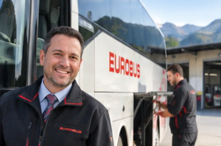 A driver in a EUROBUS jacket stands in front of a coach, a mechanic works in the background
