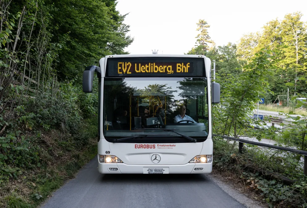 A bus showing «Uetliberg, Bhf» drives through a forest
