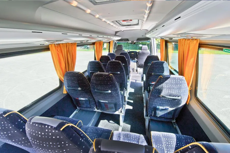 Rows of seats in the minibus with blue upholstery and orange curtains