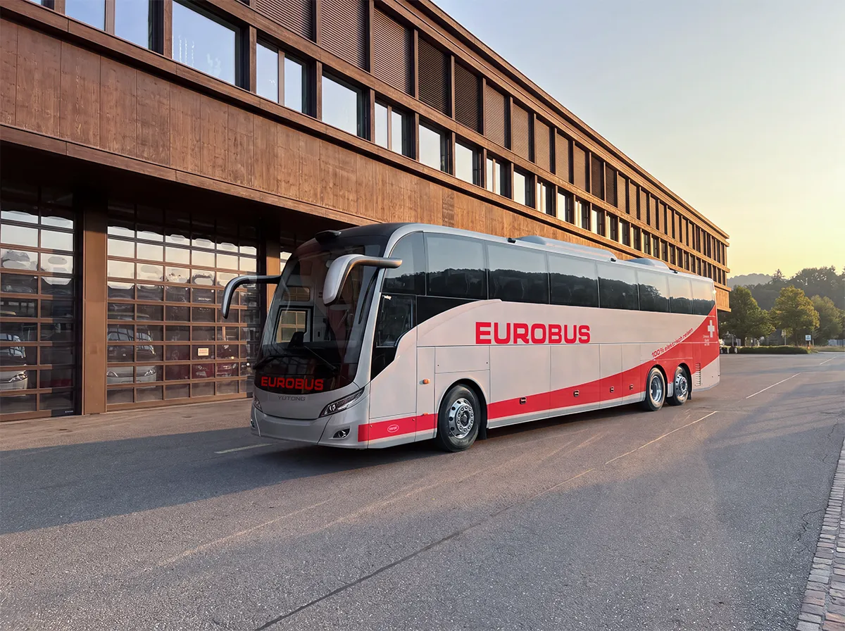 Der Elektro-Reisebus von EUROBUS steht vor einem Gebäude mit dunkler Holzfassade