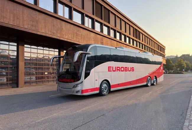 The EUROBUS electric coach parked in front of a building with a dark wooden façade