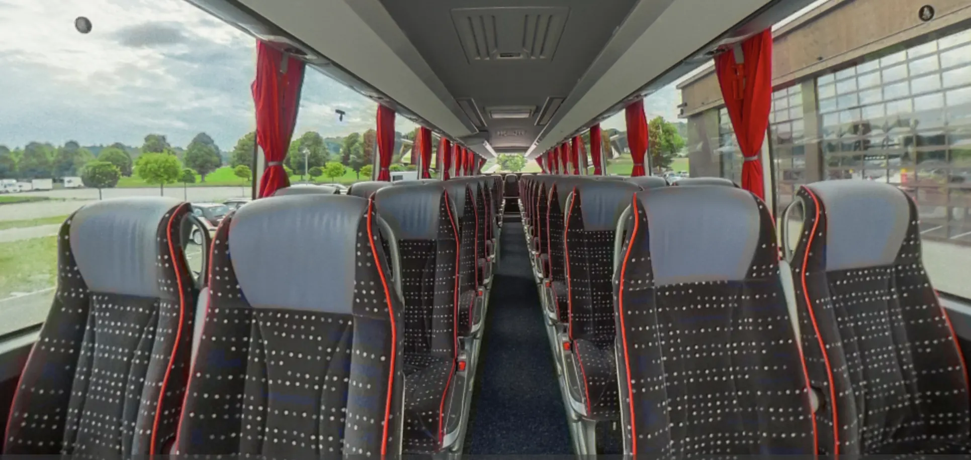 Vista lungo il corridoio centrale di un pullman con sedili fantasia e tende rosse