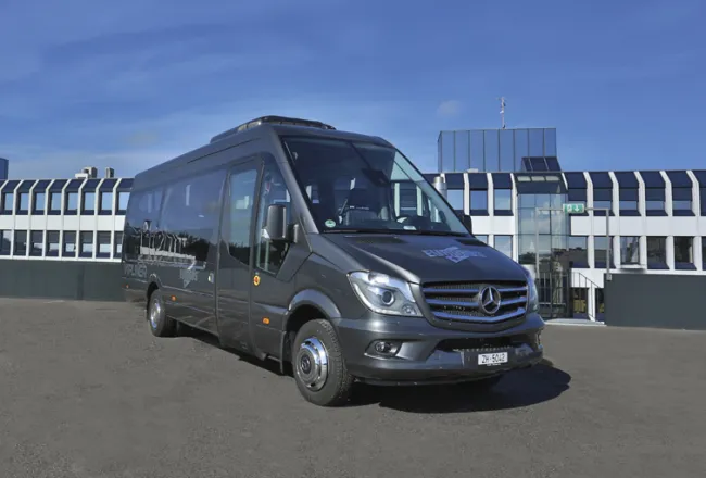 A dark VIPLINER minibus parked in front of a building with a glass front