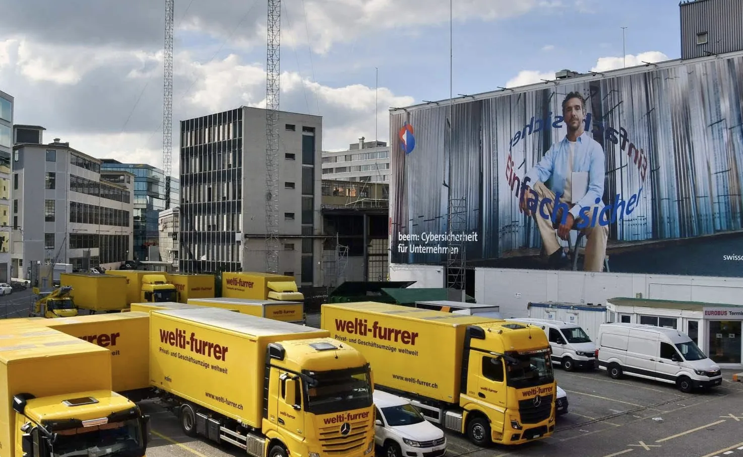 Camion e furgoni di welti-furrer nell’area aziendale, sullo sfondo un grande telone pubblicitario
