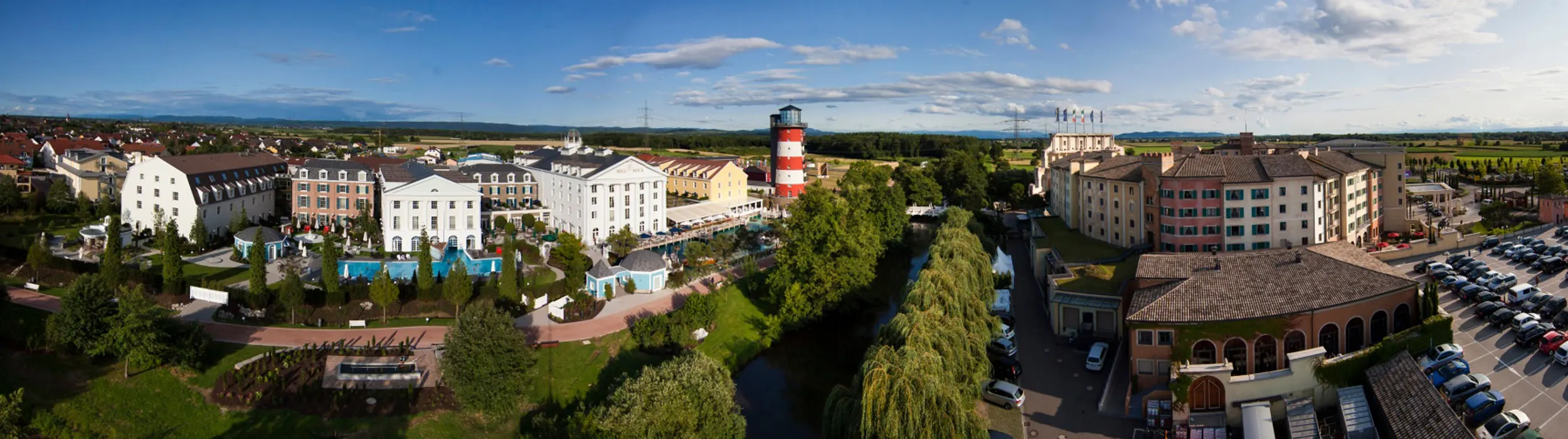 Vista dall’alto dell’Hotel Bell Rock con edifici bianchi, piscina e un faro bianco e rosso, accanto un ruscello con salici piangenti