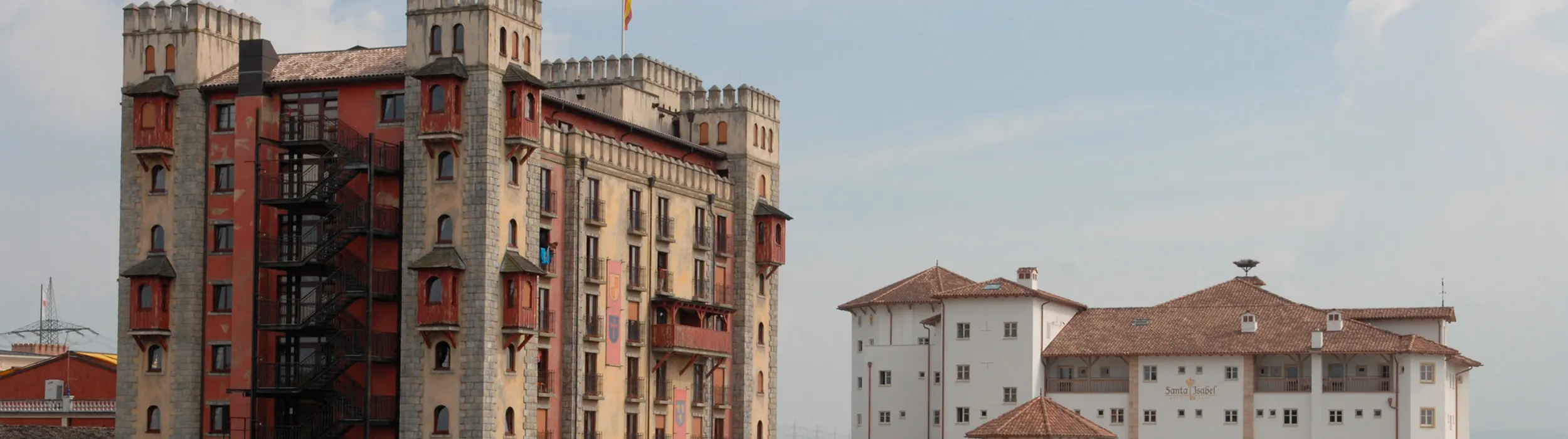 The castle of Hotel Castillo Alcazar with battlements, towers and a Spanish flag, on the right the white Hotel Santa Isabel