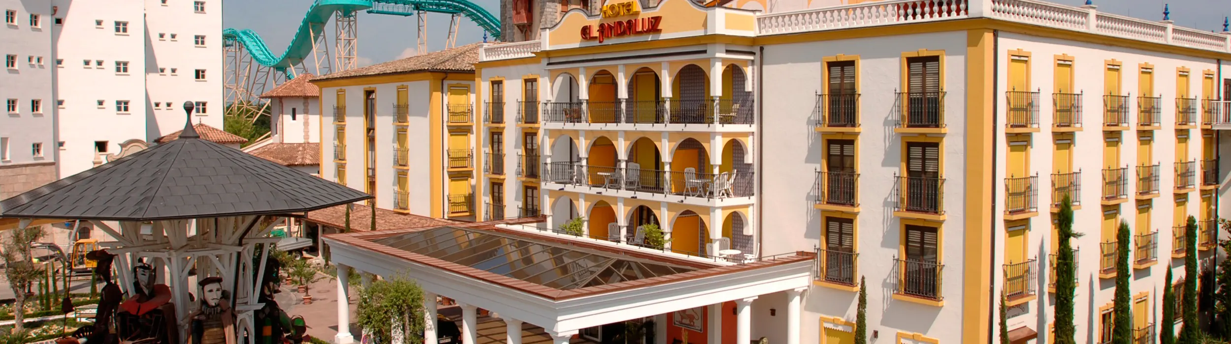 The yellow-and-white Hotel El Andaluz with arcaded balconies and lettering, in front of it a pavilion with figures, behind it a roller coaster