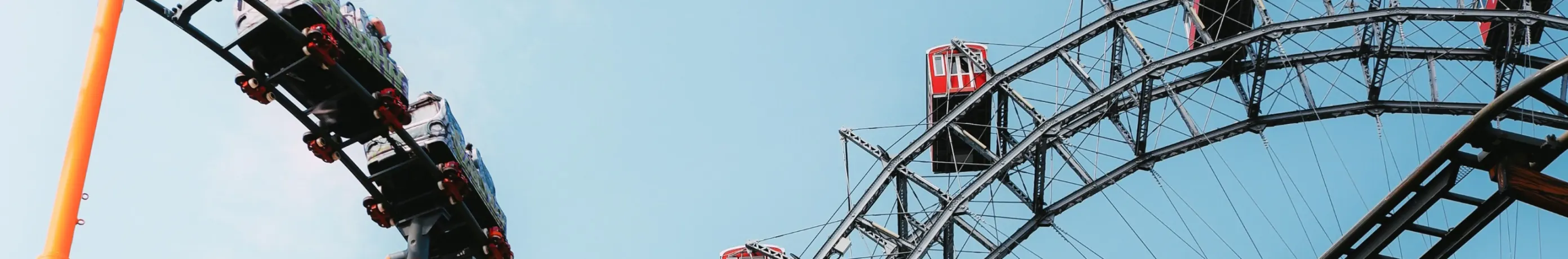 Roller coaster cars and a Ferris wheel against a blue sky