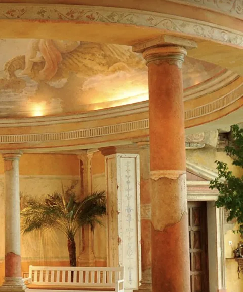 Un salone con alte colonne e una cupola dipinta in stile romano