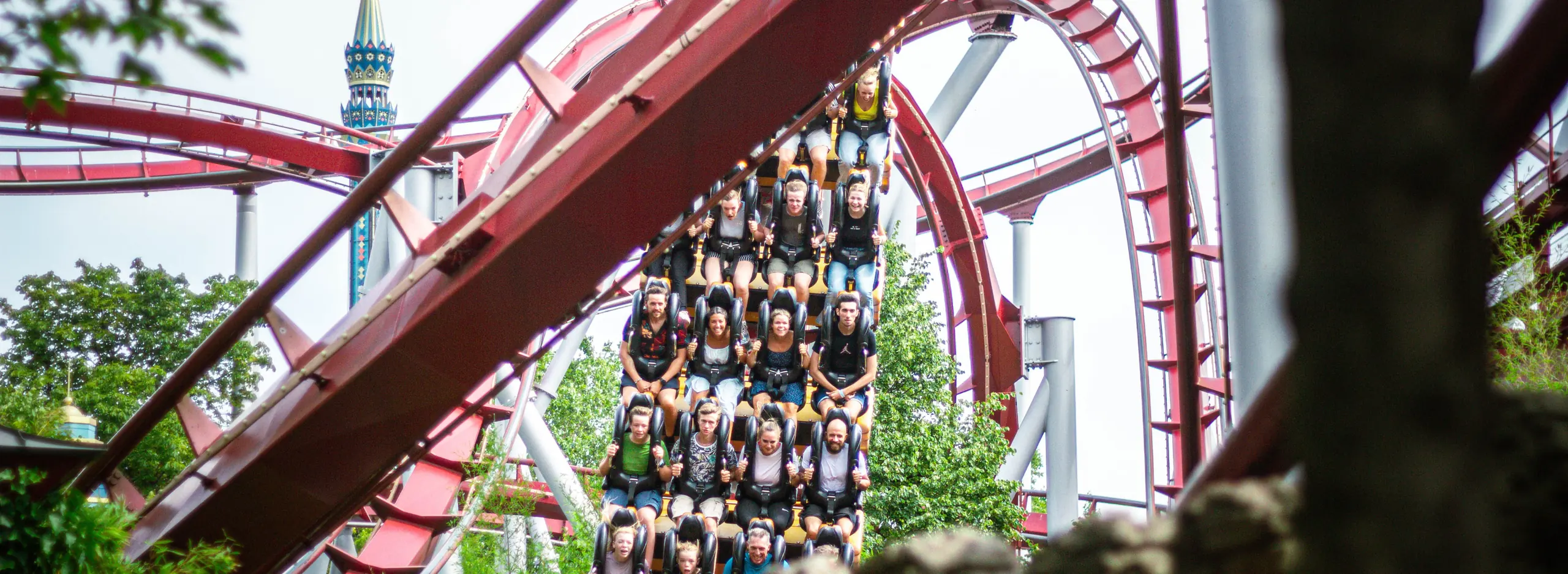 A fully occupied roller coaster train running between red track arches and trees